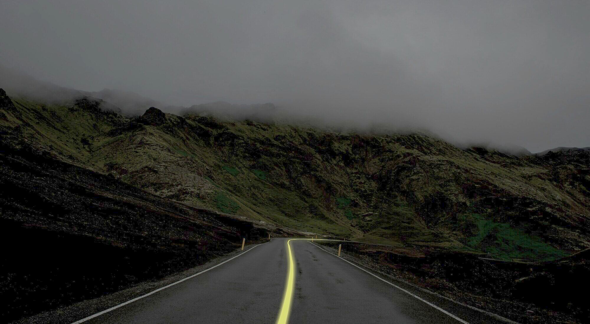 An empty road at dusk curving over a hill, a yellow line along its edge