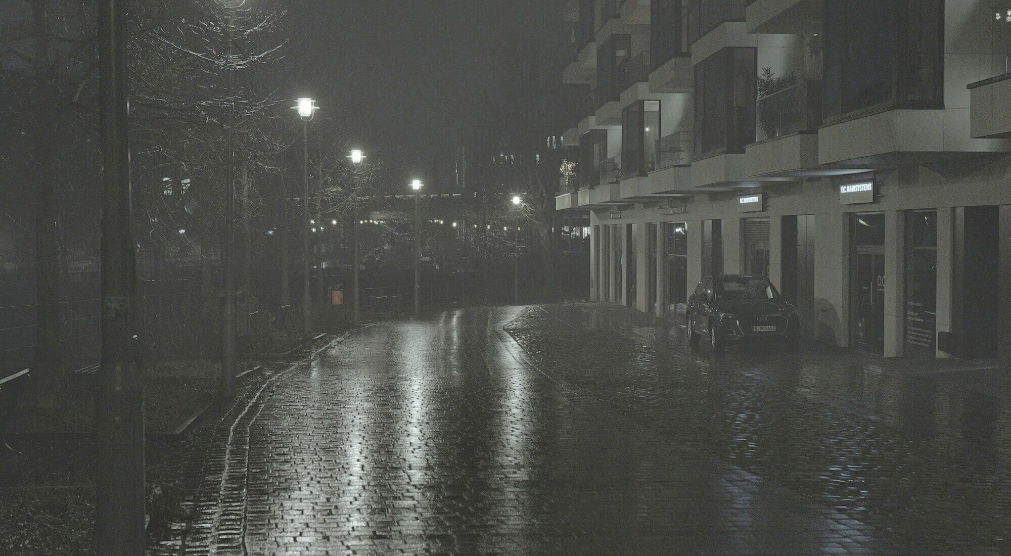 A quiet street at night after rain, streetlamps reflected in the wet paving