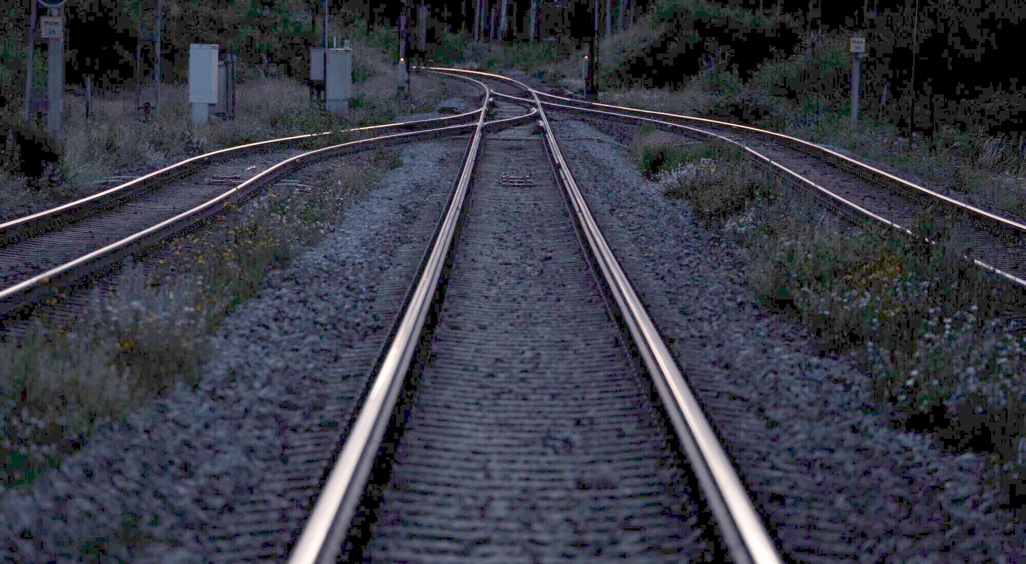 Railway tracks at night converging into the distance, the rails catching faint light